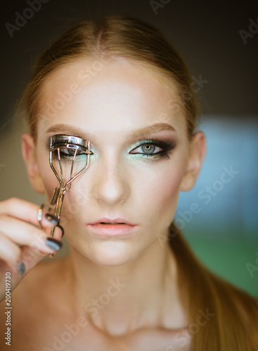 Woman corrects eyelashes with curling tongs, closeup photo