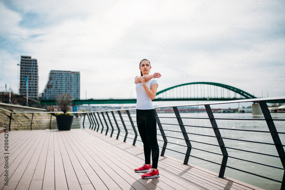 Millenial woman stretching before the run on a river bank.