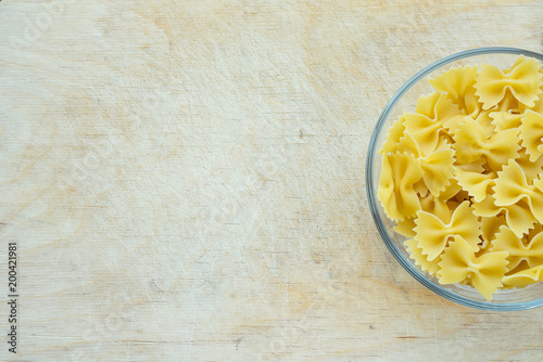 farfalle macaroni Pasta in a glass cup on a wooden table textured background with a side. Close-up with the top. With space for text.