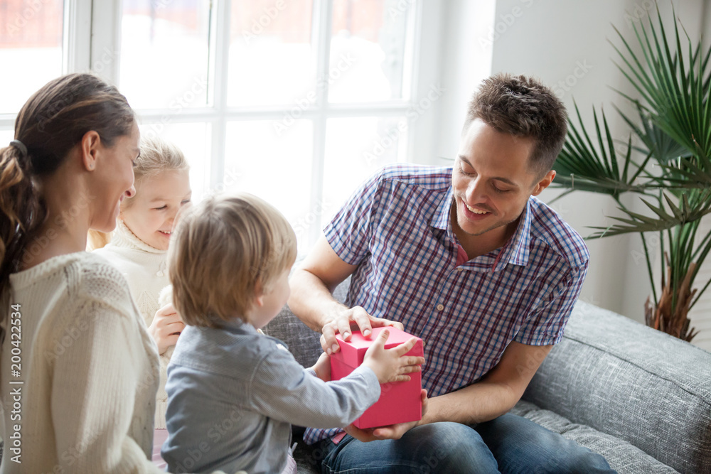 Little son presenting gift for dad, cute boy holding box making daddy surprise present, kids congratulating excited happy parent with birthday, young family celebrating fathers day together concept Little son presenting gift for dad, cute boy holding box making daddy surprise present, kids congratulating excited happy parent with birthday, young family celebrating fathers day together concept