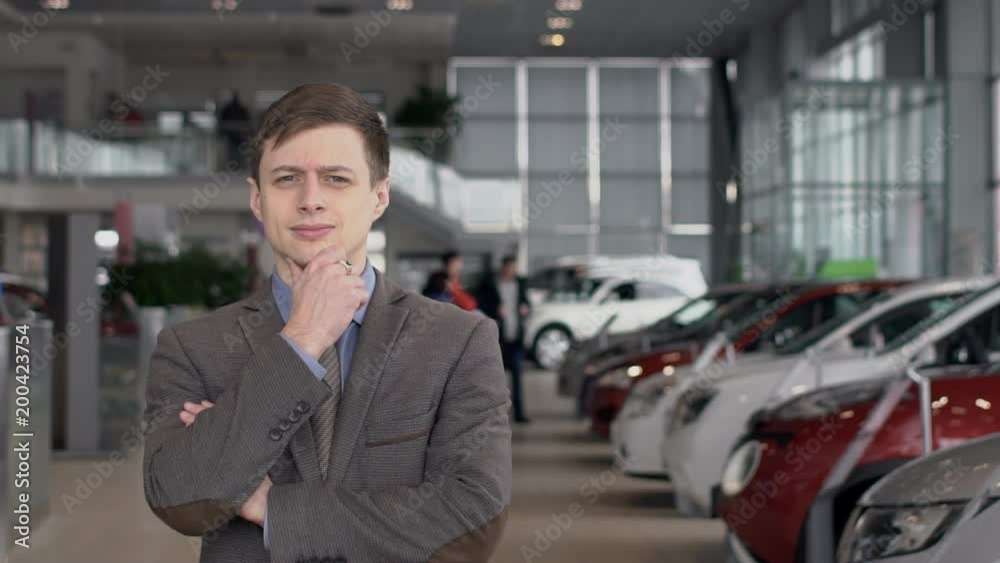 Portrait of young businessman standing in autocenter, slow motion. Concept: people, auto, machine Portrait of young businessman standing in autocenter, slow motion. Concept: people, auto, machine