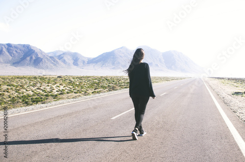 young woman with long hair walks alone on a long straight road