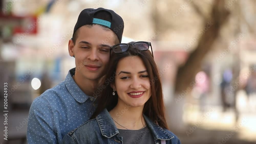 Portrait of a tender young woman with beautiful long loose hair and her young boyfriend smiling romantically and standing in an airy alley in spring Portrait of a tender young woman with beautiful long loose hair and her young boyfriend smiling romantically and standing in an airy alley in spring