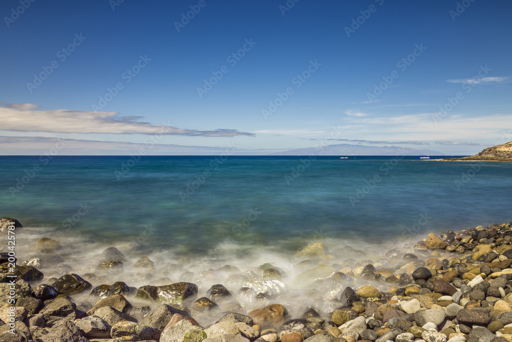 Stony beach with long exposure water and La Gomera on the horizon Stony beach with long exposure water and La Gomera on the horizon