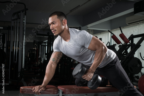 Muscular builder man training his body with dumbbell in Modern fitness center