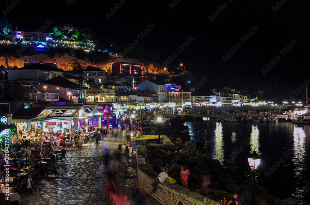 Parga, Epirus - Greece. Nightlife in Parga town during the summer. Tourists enjoying their holidays having a drink, eating greek traditional food or walking at the paved alley by the sea