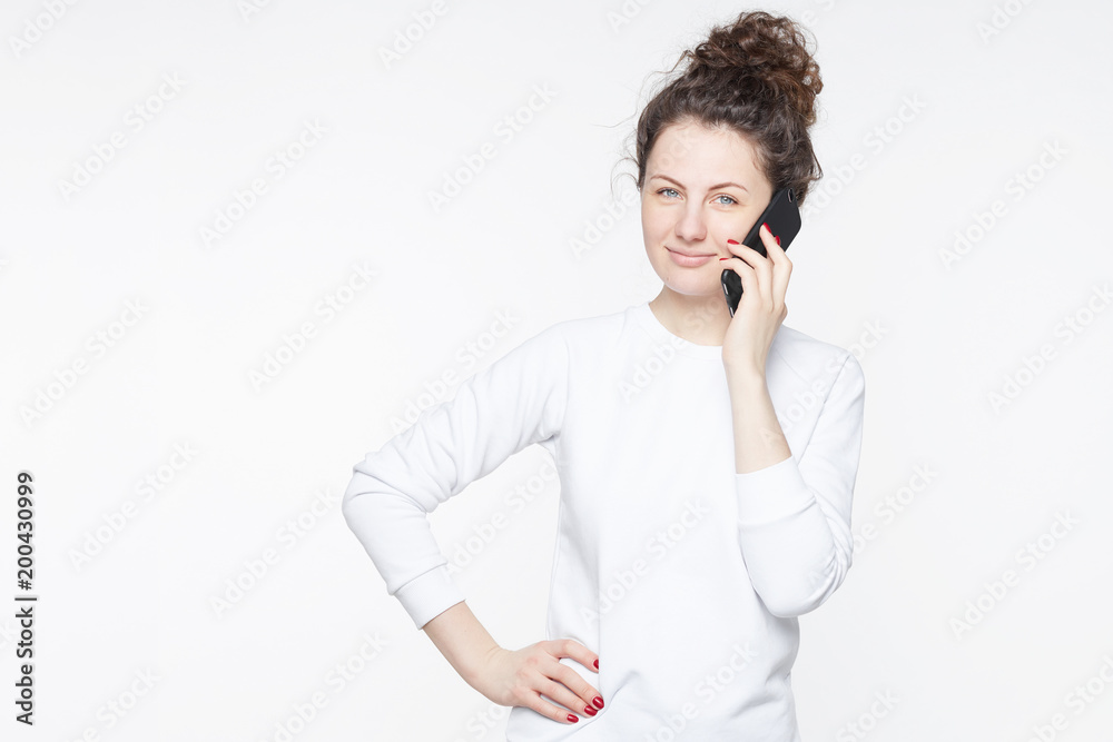 Studio portrait of cute American brunette businesswoman with bushy hairstyle calling abroad to partner, making appointment, listening attentively, looking at camera with confident face expression. Studio portrait of cute American brunette businesswoman with bushy hairstyle calling abroad to partner, making appointment, listening attentively, looking at camera with confident face expression.