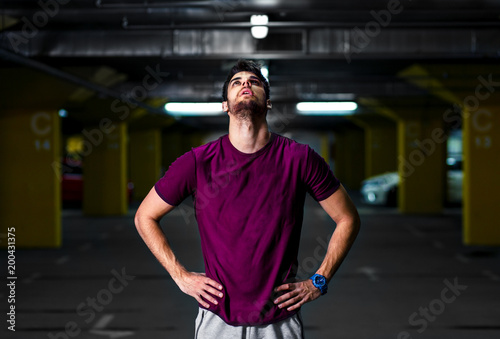  Young athlete man resting after workout in the underground car parking.