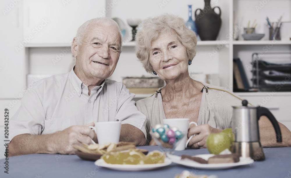 Smiling elderly spouses enjoying tea with sweets