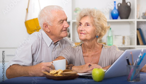 Happy elderly pair using laptop at home