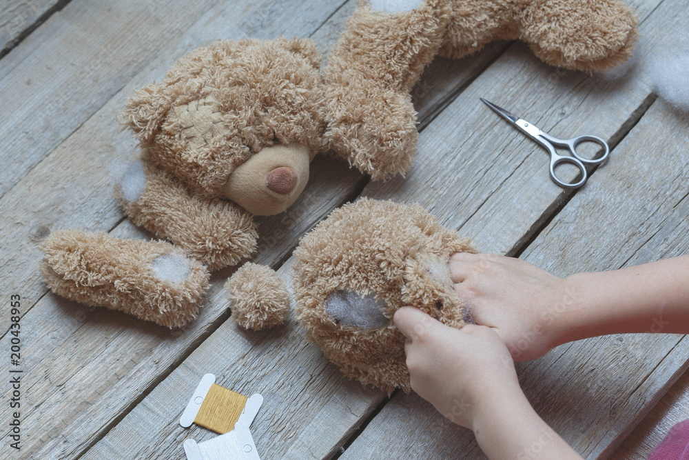 A girl sews a bear toy. Handicraft with children. Child fills the toy with a sintepon. - obrazy, fototapety, plakaty 