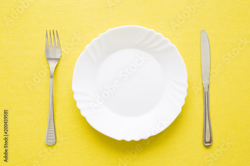 Clean  empty  white plate  fork and knife with yellow tablecloth on a table. Cutlery concept. Flat lay. Top view.