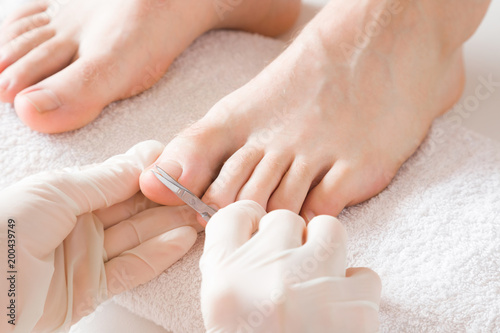 Pedicurist's hands in protective rubber gloves cutting toenails with scissors. Cares about man's feet. Specialist with client in beauty salon. Professional beauty service. Pedicure, manicure concept. photo