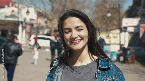 Portrait of a stylish and successful young woman with long loose hair smartening up and smiling cheerfully outdoors in spring in slow motion photo