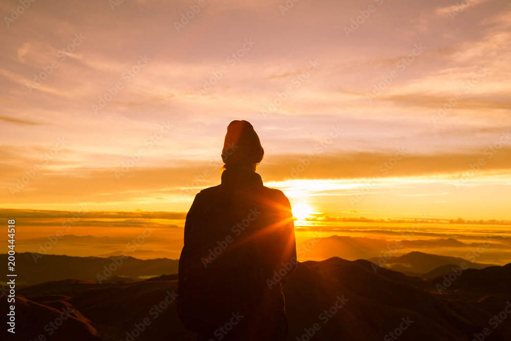 woman reaching the top of the mountain to see the golden sunset. 