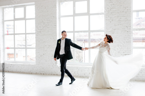Wedding couple dancing by the big window in the studio with a white interior.