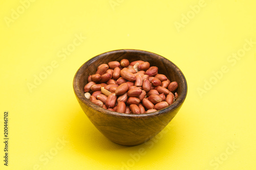 Peanuts on wooden bowl on yellow background