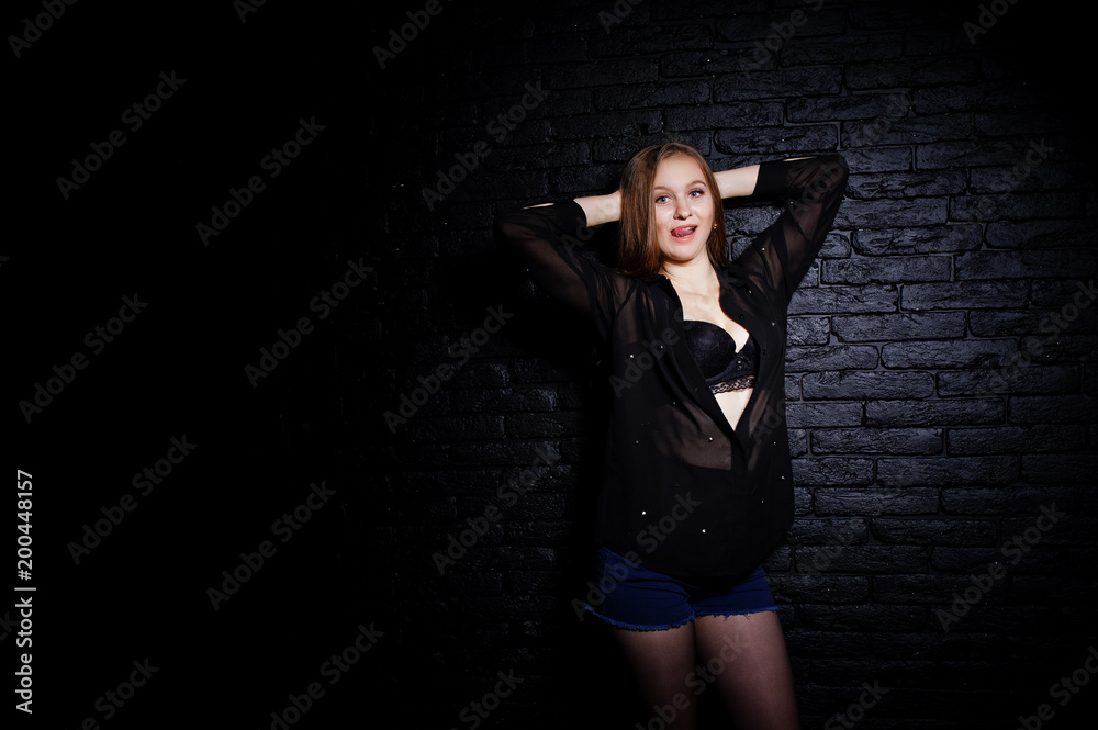 Studio shot of brunette girl in black blouse with bra and shorts against black brick wall. Studio shot of brunette girl in black blouse with bra and shorts against black brick wall.