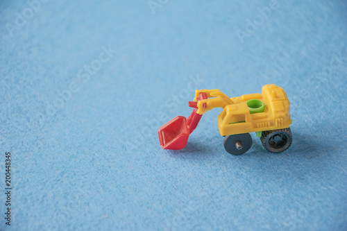 Small decorative toy excavator on blue background. Macro abstract photo. Construction, mining, construction equipment at work