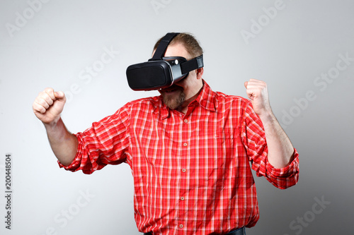 Portrait of bearded man watching virtual reality glasses over gray background with copyspace.