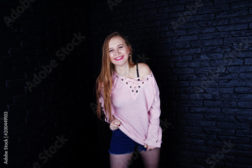 Studio shot of brunette girl at pink sweater with jeans shorts against black brick wall. © AS Photo Family