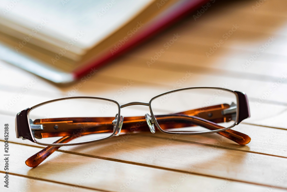 Open book and glasses on wooden table close Open book and glasses on wooden table close