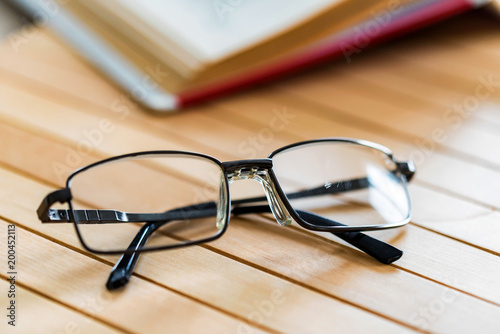 Open book and glasses on wooden table close