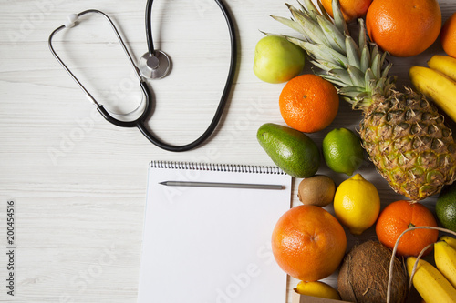 Stethoscope health diet. Different fruits with notepad on white wooden background. Flat lay. Top view. Copy space.