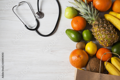 Stethoscope health diet. Different fruits on white wooden background. Flat lay. Top view. Copy space.
