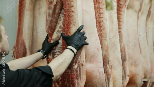 back view of butcher man working in slaughter house near carcasses of pigs in row meat factory dead pig pork meat consumerism food business enterprise hanging dead domestic animals human cruelty