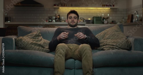 Man walks into the living room and sits on a couch to watch tv