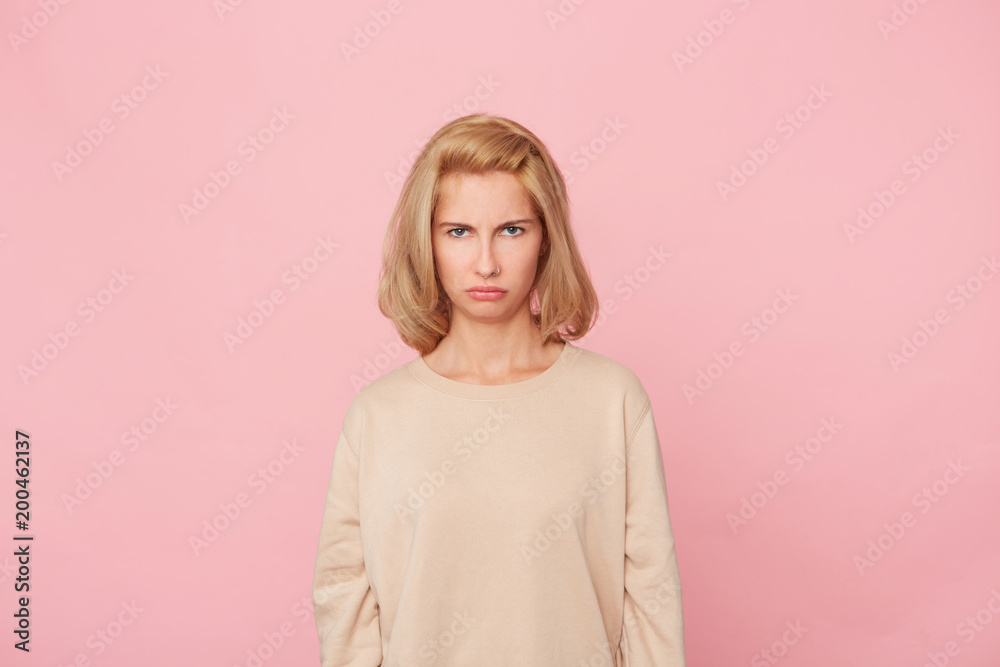 Indoor shot of blonde discontent dissatisfied young woman feels andgry and sinister because offended by her boyfriend. Facial expression and negative emotions. Isolated over pink background