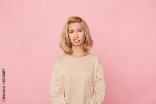 Indoor shot of shocked beautiful young woman, keep up her lip and feels bewildered and blank. Isolated over pink background © timtimphoto