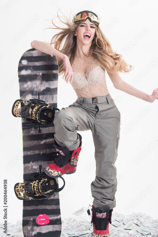 Snowboard girl. Winter, leisure, extreme sport and people concept - woman  in ski goggles with very expressive emotion holds snowboard. Attractive  athletic woman wears sexy clothes, standing on dollars Stock Photo