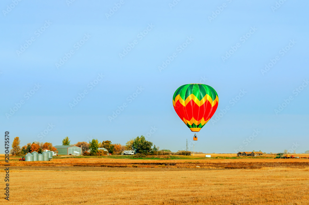 Fototapeta premium A multi-colored balloon is flying over a field in the sky near a farm