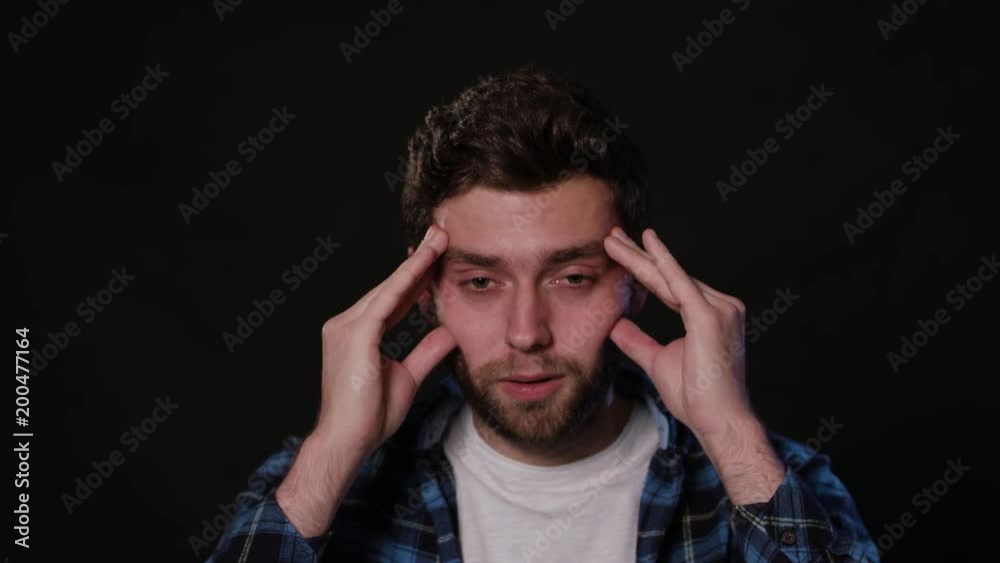 A young man immitating a headache against a black background. Close-up Shot A young man immitating a headache against a black background. Close-up Shot