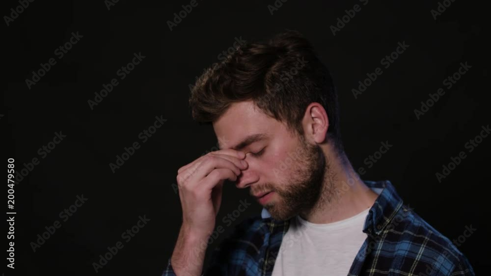 A young man immitating a headache against a black background. Close-up Shot A young man immitating a headache against a black background. Close-up Shot