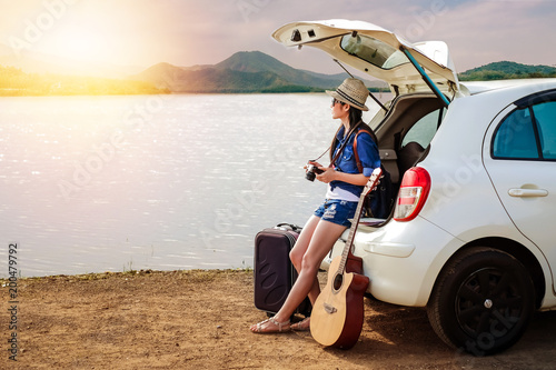 woman traveler sitting on hatchback of car and looking to local map near the lake during holiday background is the mountain.Young lady tourist enjoying for view of nature on vacation. 
