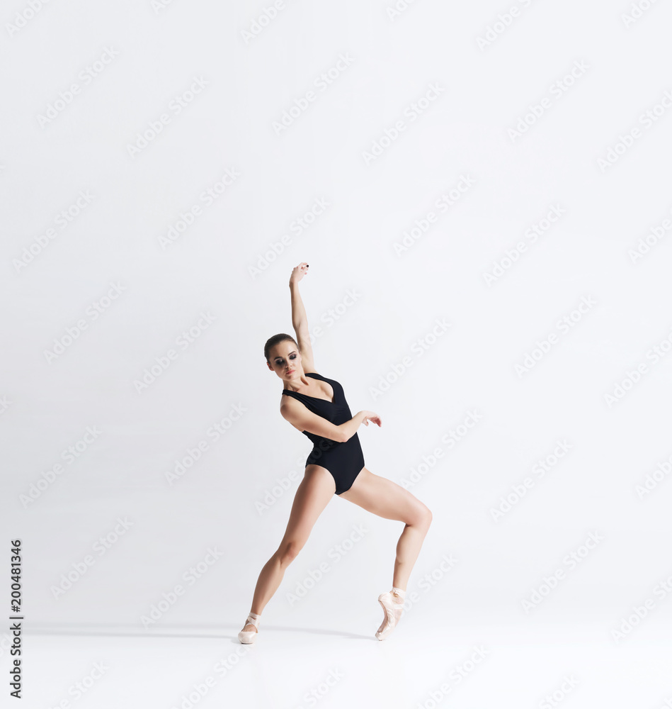 Ballerina in point shoes and bodysuit is dancing in studio.