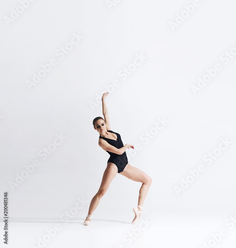 Ballerina in point shoes and bodysuit is dancing in studio.