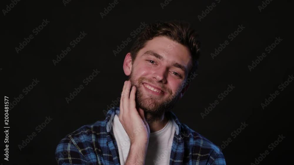 A young man touching his beard against a black background. Close-up Shot A young man touching his beard against a black background. Close-up Shot