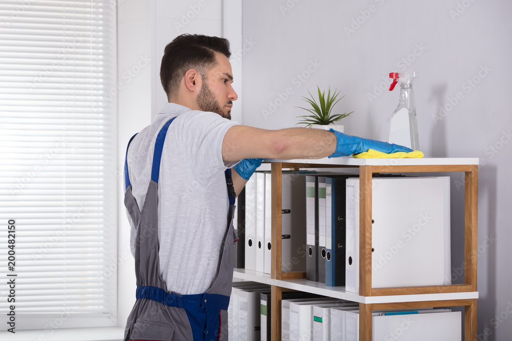 Male Cleaner Cleaning Shelf At Workplace