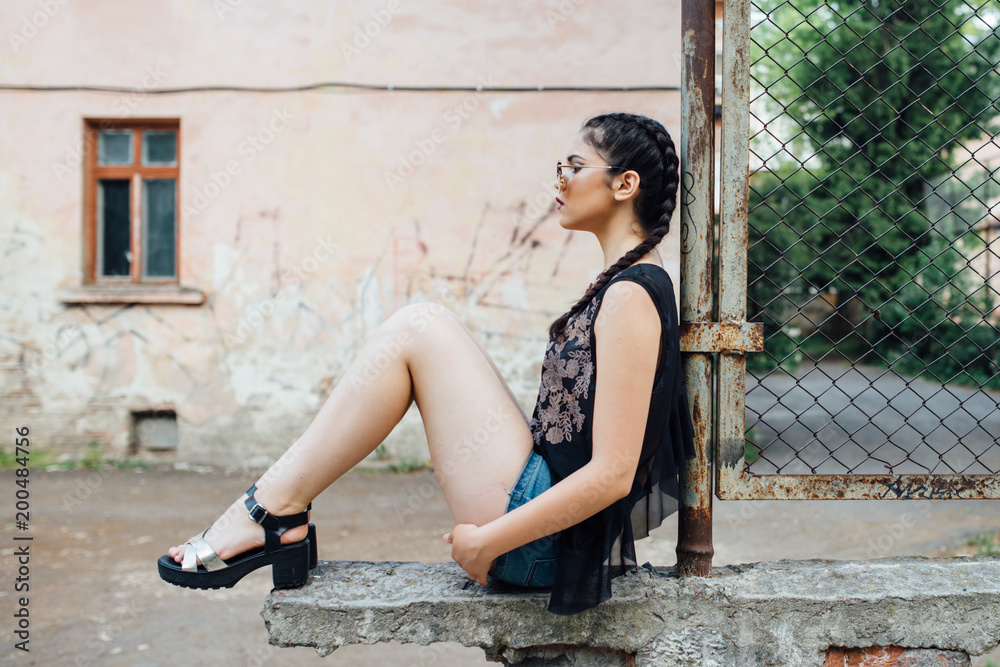 A young pretty girl sitting on a fence wall and thinking