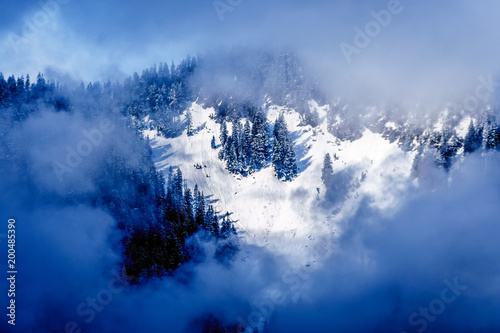 Sun shining through the clouds on the Snow Capped Peak of Coquitlam Mountain in the Coast Mountain Range seen from the shore of Pitt Lake in the Fraser Valley of British Columbia, Canada photo