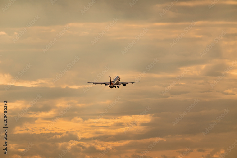 The big airliner is flying away. Colorful sky with airplane. Traveling exotic.