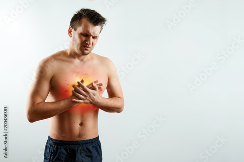 A man holds his hands and region of the heart, chest pain, a pain in the heart highlighted in red, a heart attack. Light background. The concept of medicine, massage, physiotherapy, health. photo