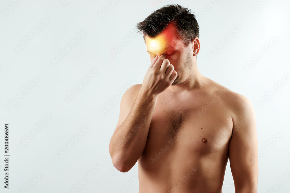 A man clings to the bridge of the nose, a headache highlighted in red, migraine. Light background. The concept of medicine, massage, physiotherapy, health.