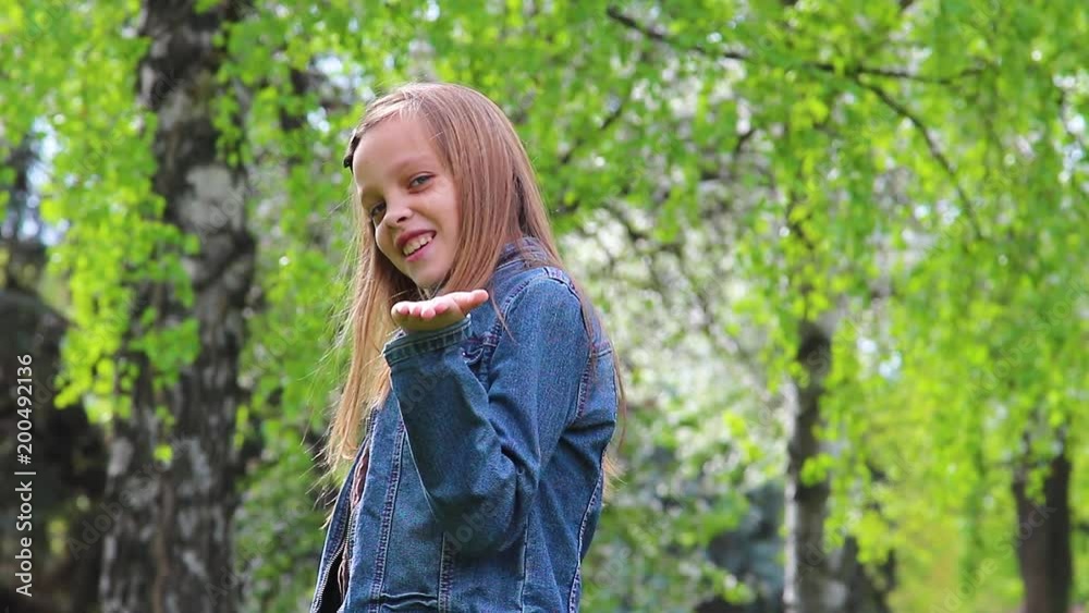 Portrait of pretty blonde teenage girl blowing kiss into camera. Teenager standing in green city park outdoors on warm spring day. Portrait of pretty blonde teenage girl blowing kiss into camera. Teenager standing in green city park outdoors on warm spring day.