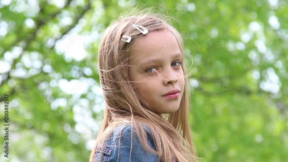 Closeup portrait of pretty teenage girl looking at camera. White happy smiling kid with natural blonde long hair standing outdoors on windy spring day.