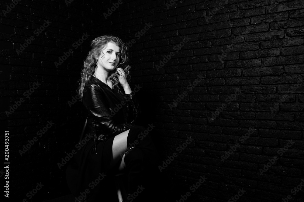Curly hair girl at leather jacket on studio against black brick wall.